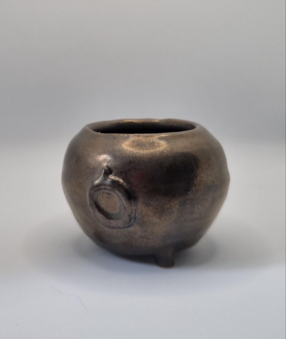 A bronze cauldron shaped tealight holder on a neutral background