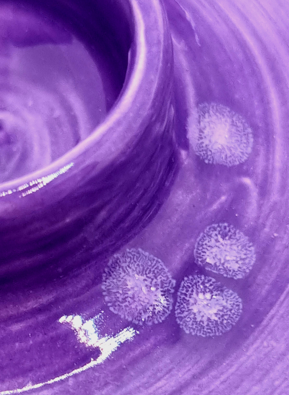 A close up of the patina of a purple candlestick on a neutral background