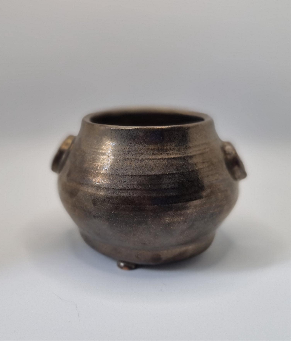 A bronze cauldron shaped tealight holder on a neutral background