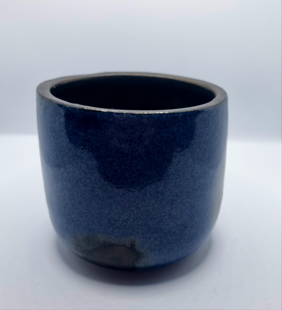 A dark blue & bronze ceramic tumbler on a neutral background