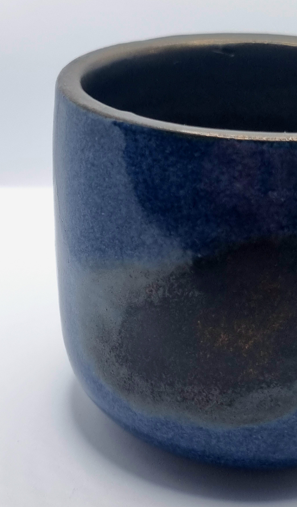 Close up of a dark blue & bronze ceramic tumbler on a neutral background