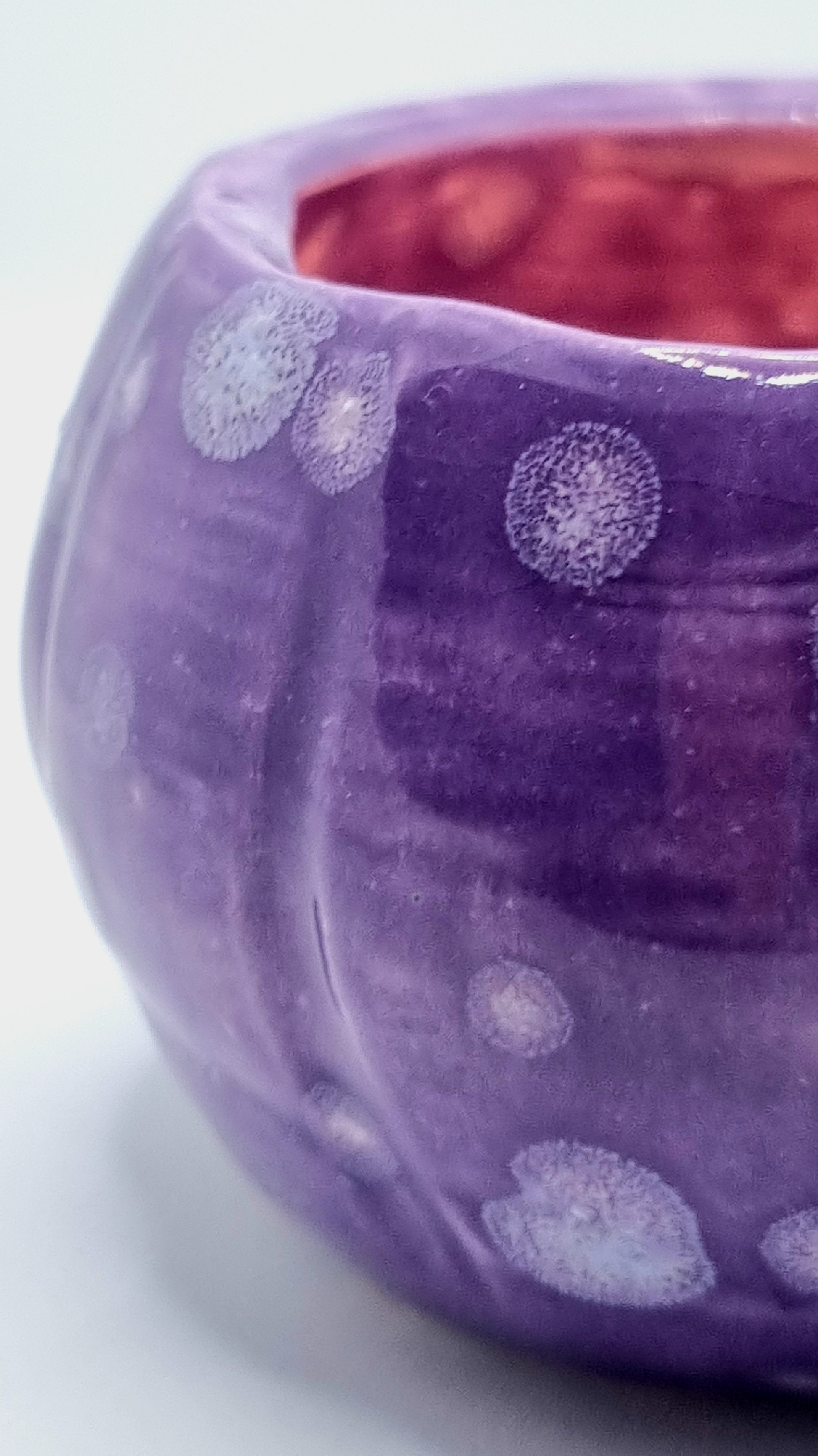 Close up of the patina of a purple, pumpkin-shaped tealight holder with a lit tealight inside on a neutral background