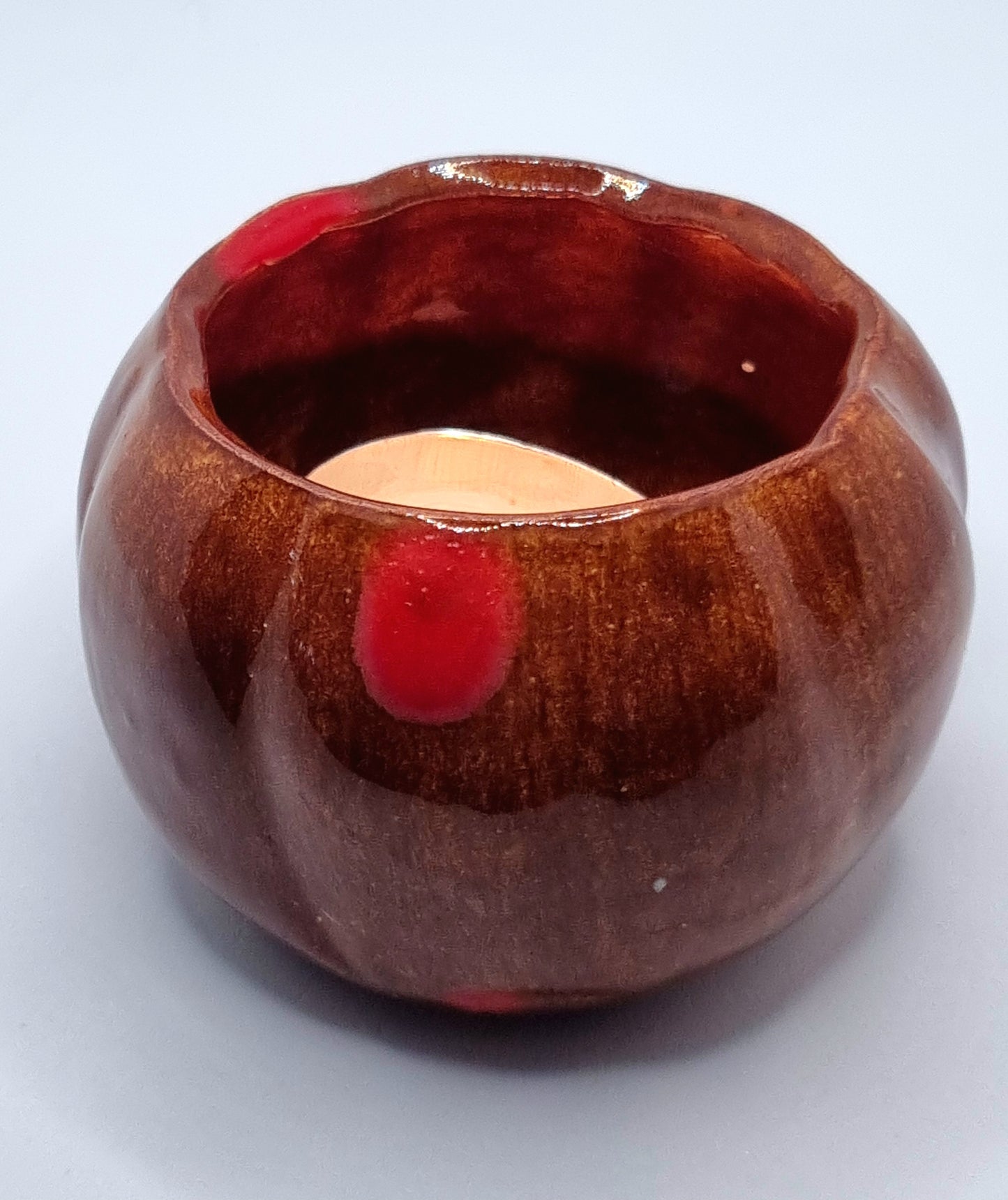 An orange pumpkin-shaped tealight holder with a lit tealight inside on a neutral background