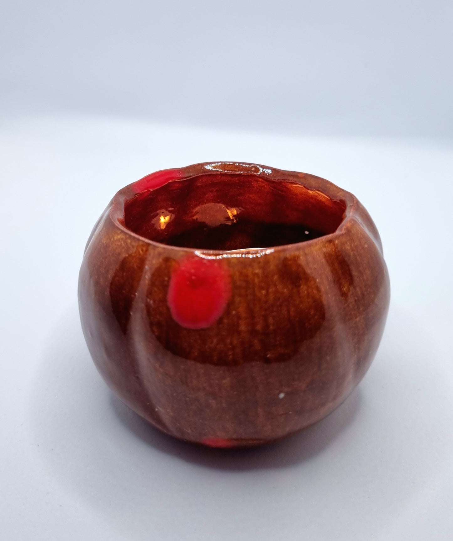 An orange pumpkin-shaped tealight holder with a lit tealight inside on a neutral background