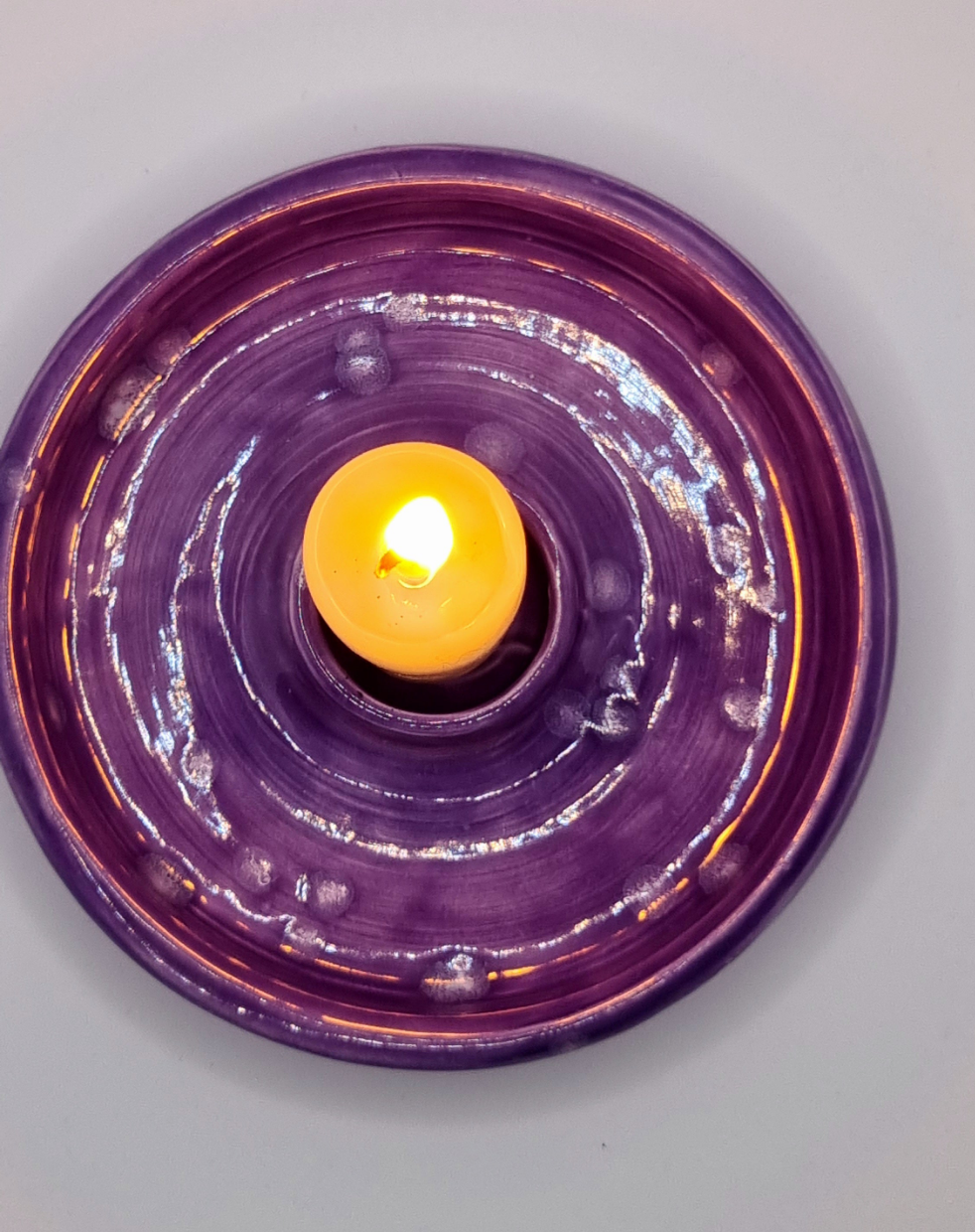 A purple candlestick from above with a lit candle on a neutral background