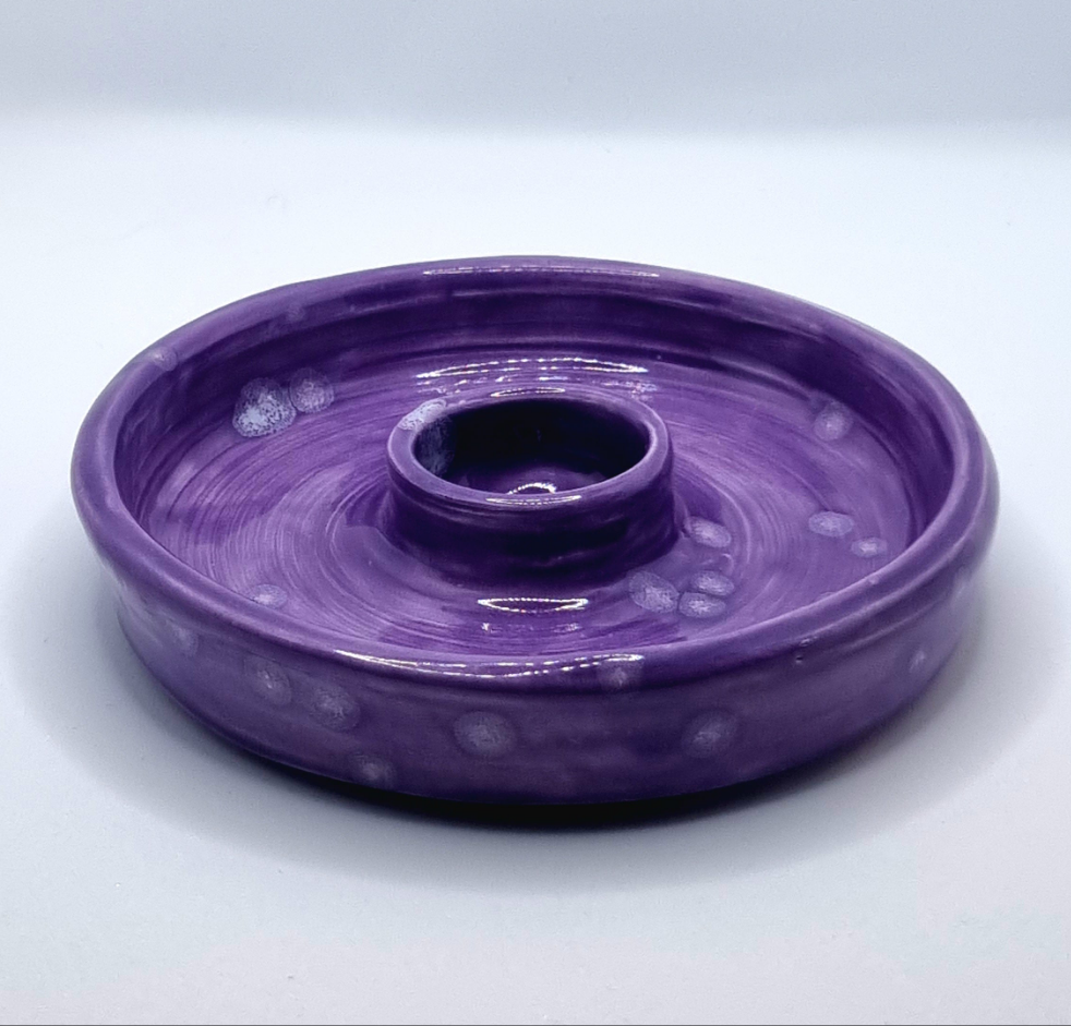 A purple candlestick with a lit candle on a neutral background