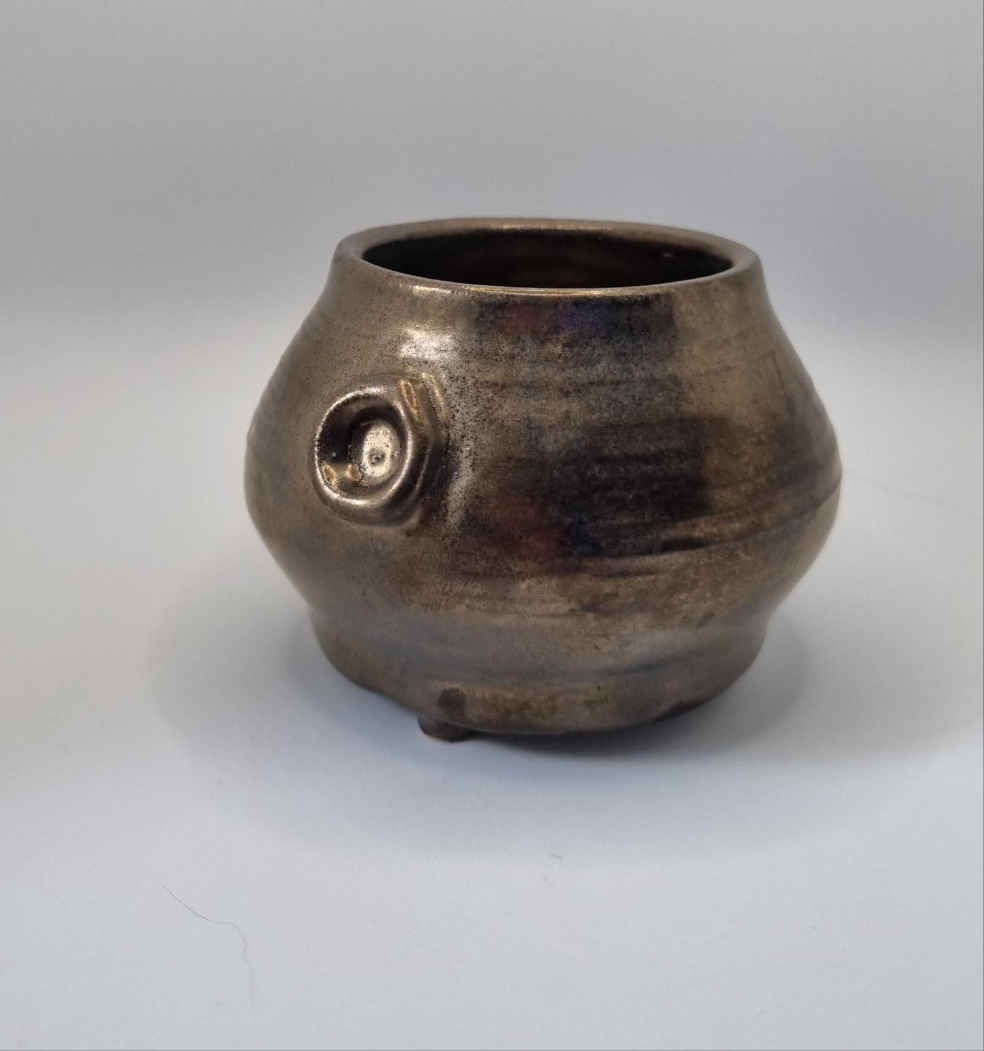 A bronze, cauldron shaped tealight holder on a neutral background 