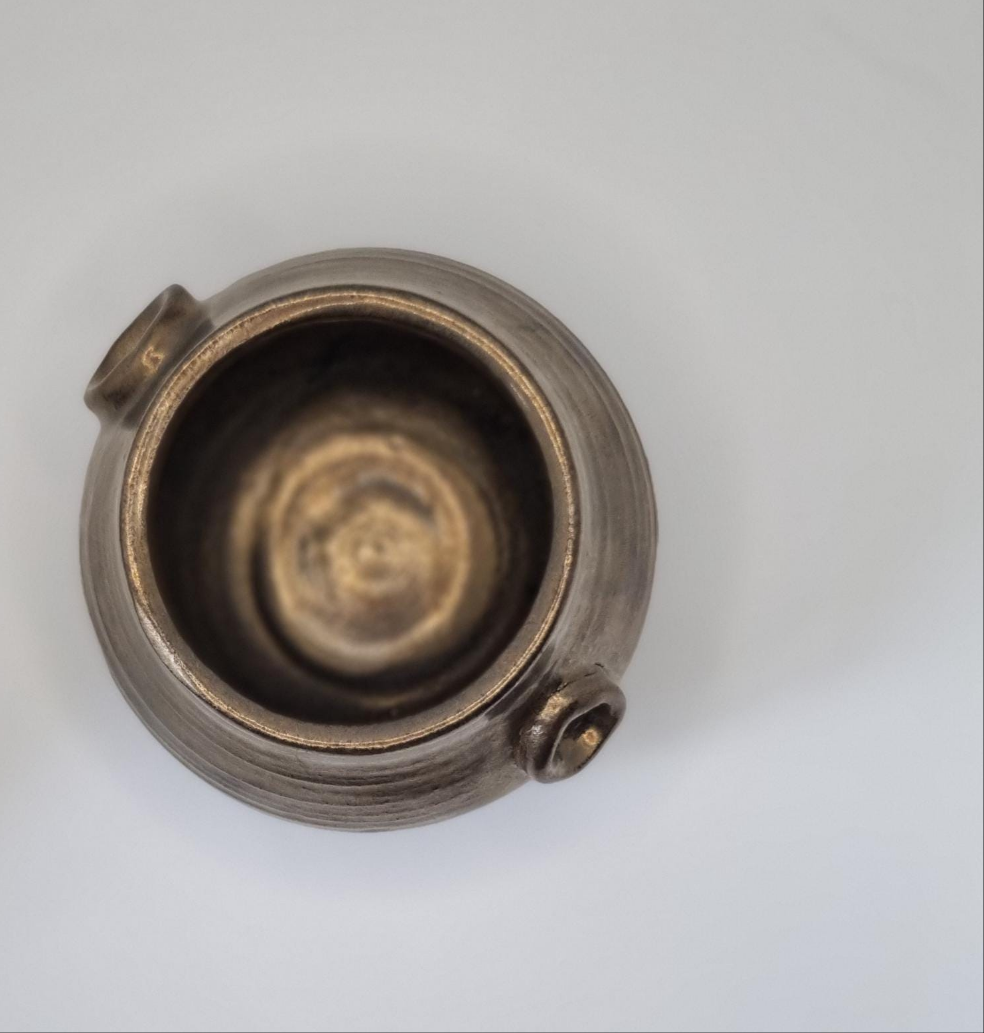 A bronze cauldron shaped tealight holder from above on a neutral background