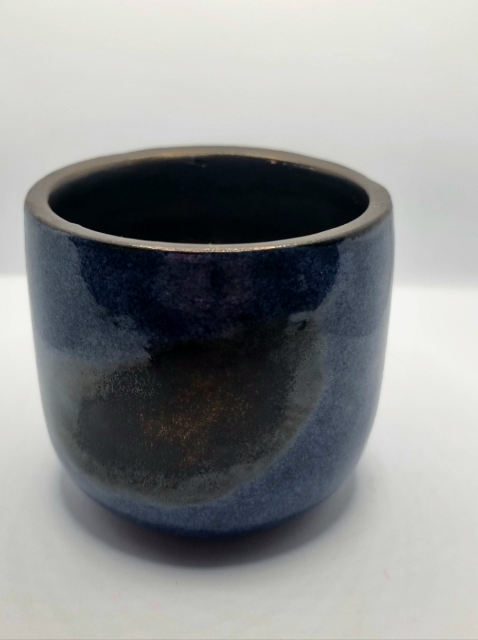 A dark blue & bronze ceramic tumbler on a neutral background 