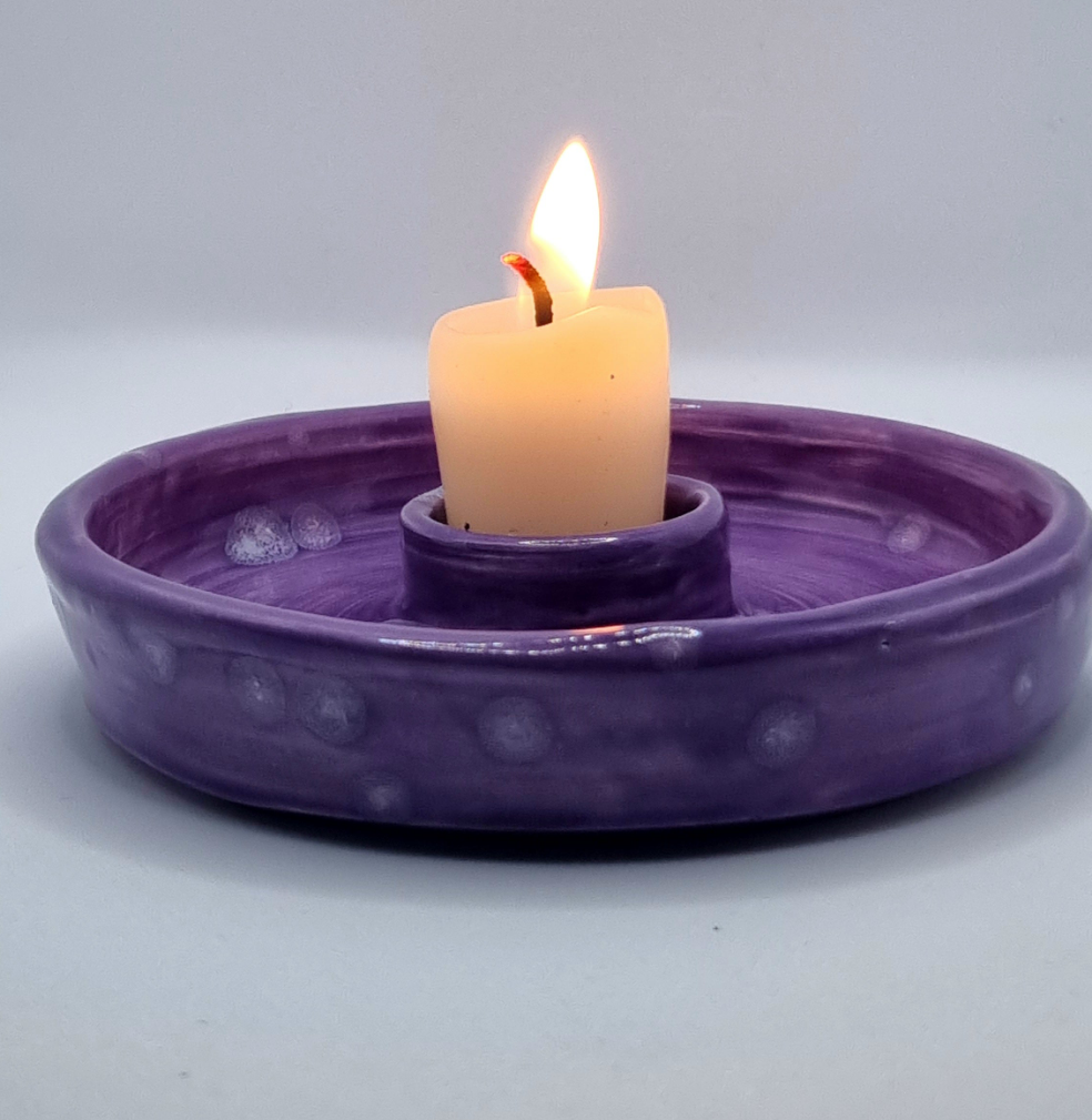 A purple candlestick with a lit candle on a neutral background
