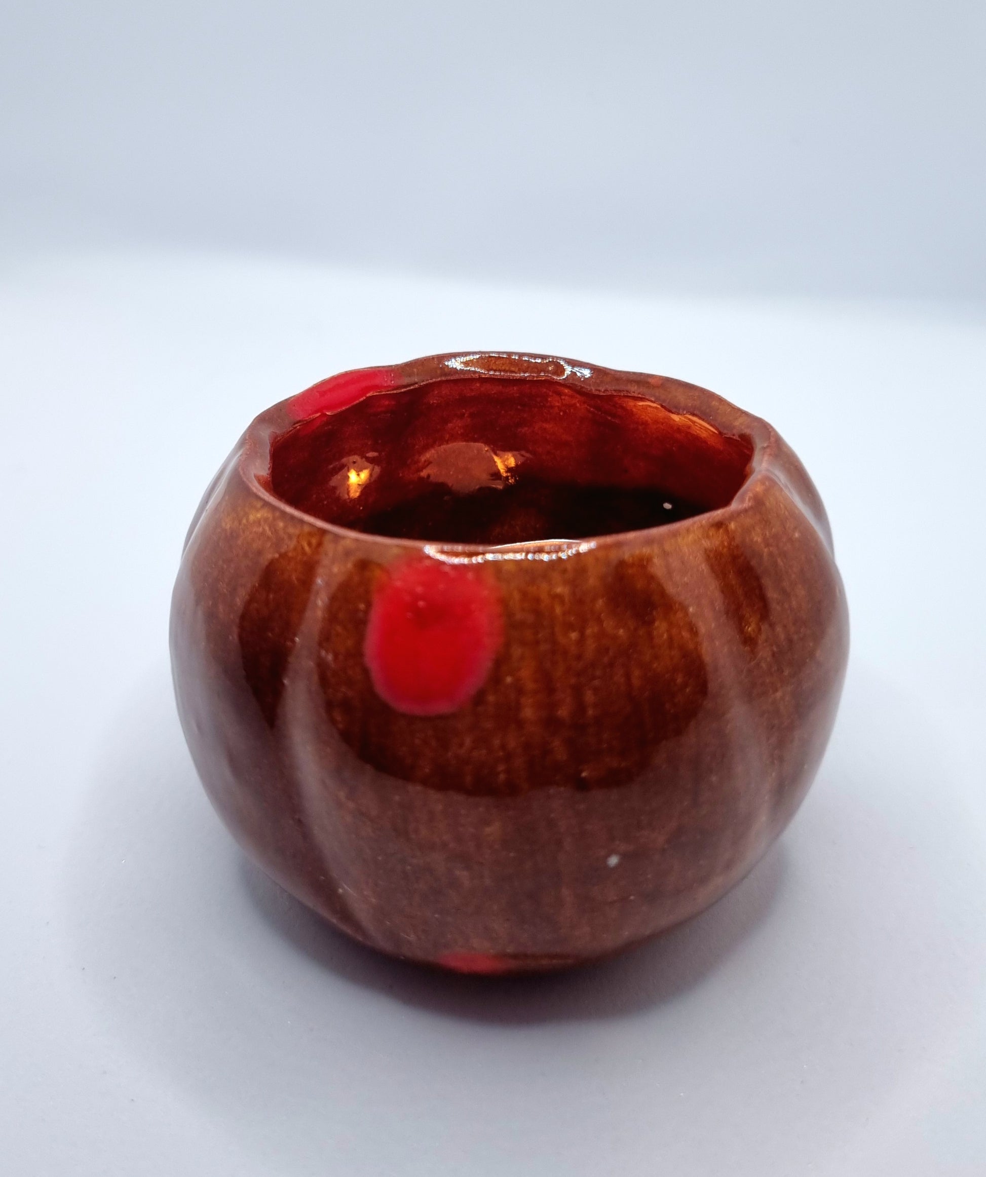An orange pumpkin-shaped tealight holder with a lit tealight inside on a neutral background 