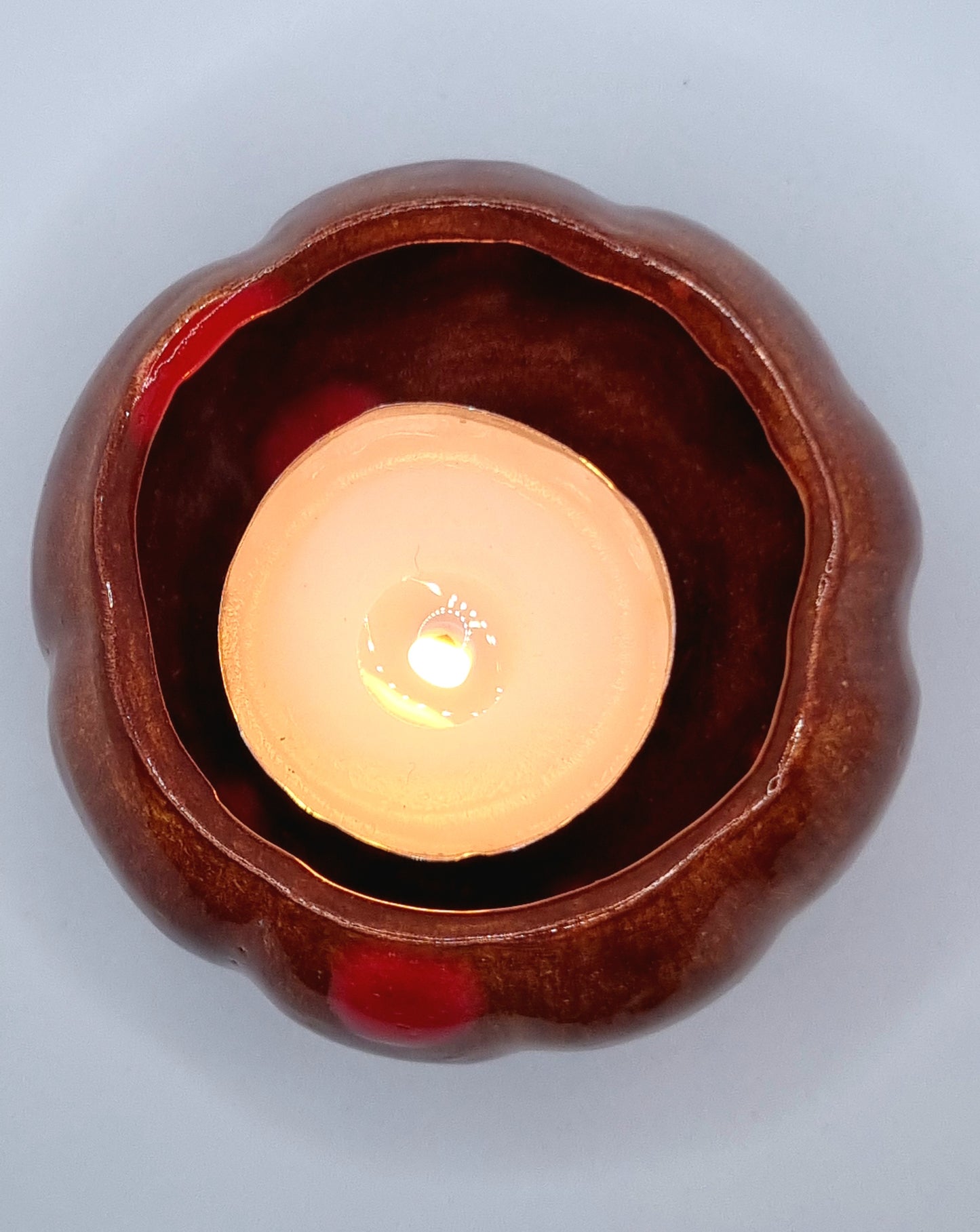 An orange pumpkin-shaped tealight holder from above with a lit tealight inside on a neutral background 