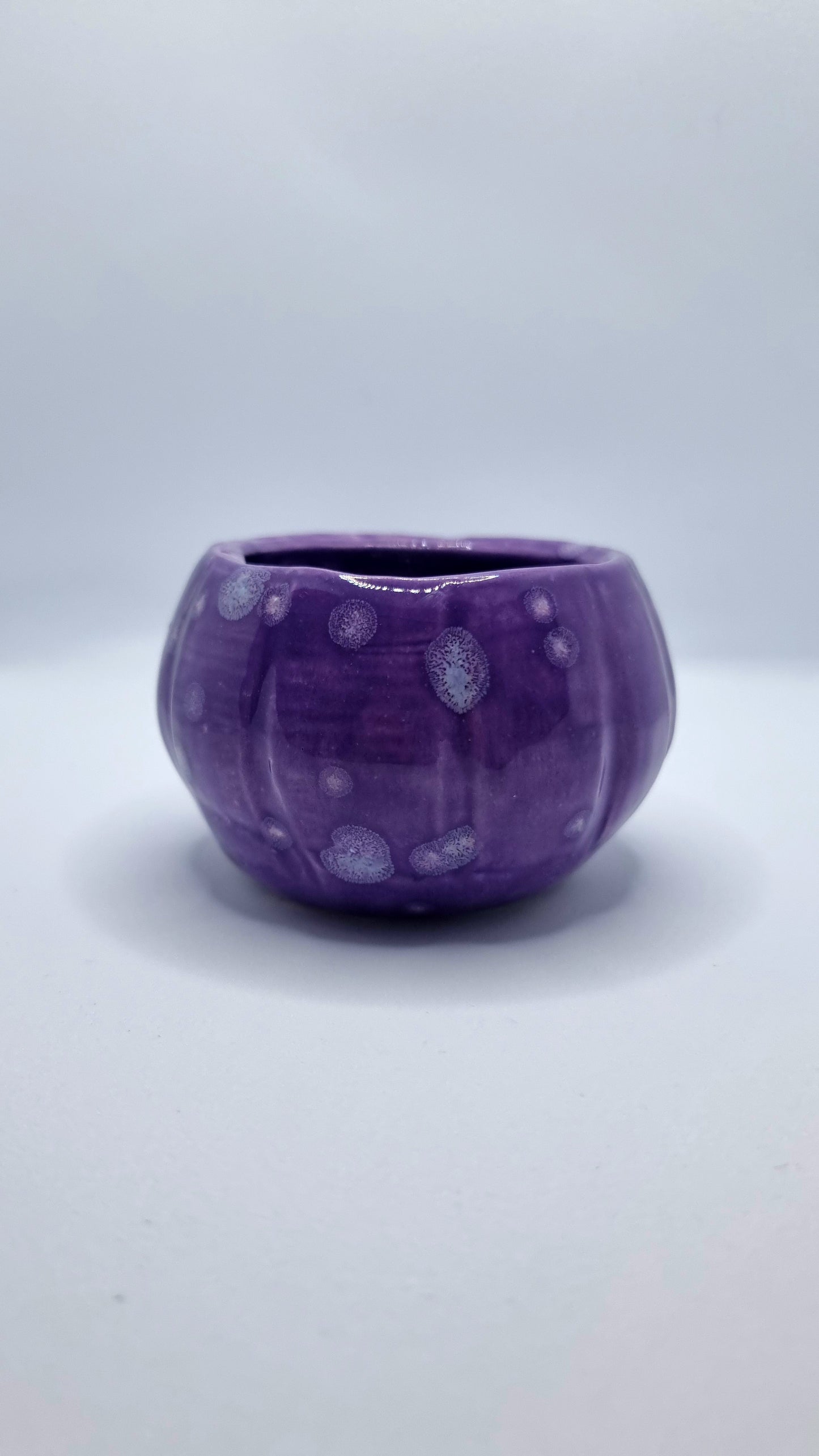 A purple, pumpkin-shaped tealight holder on a neutral background