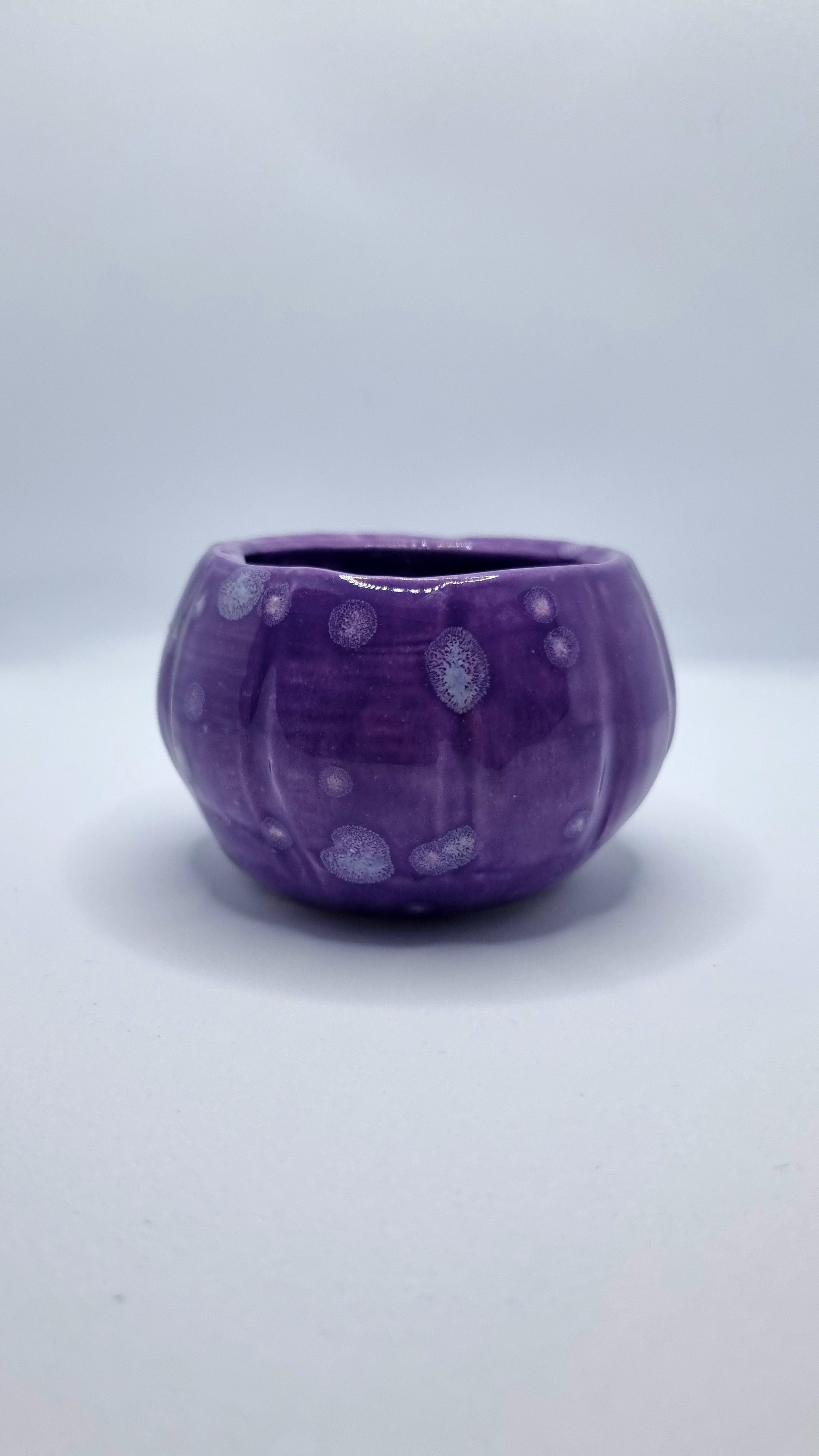 A purple, pumpkin-shaped tealight holder on a neutral background
